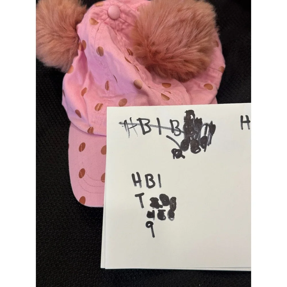 Pink polka-dot cap topped with two fluffy faux fur pom poms